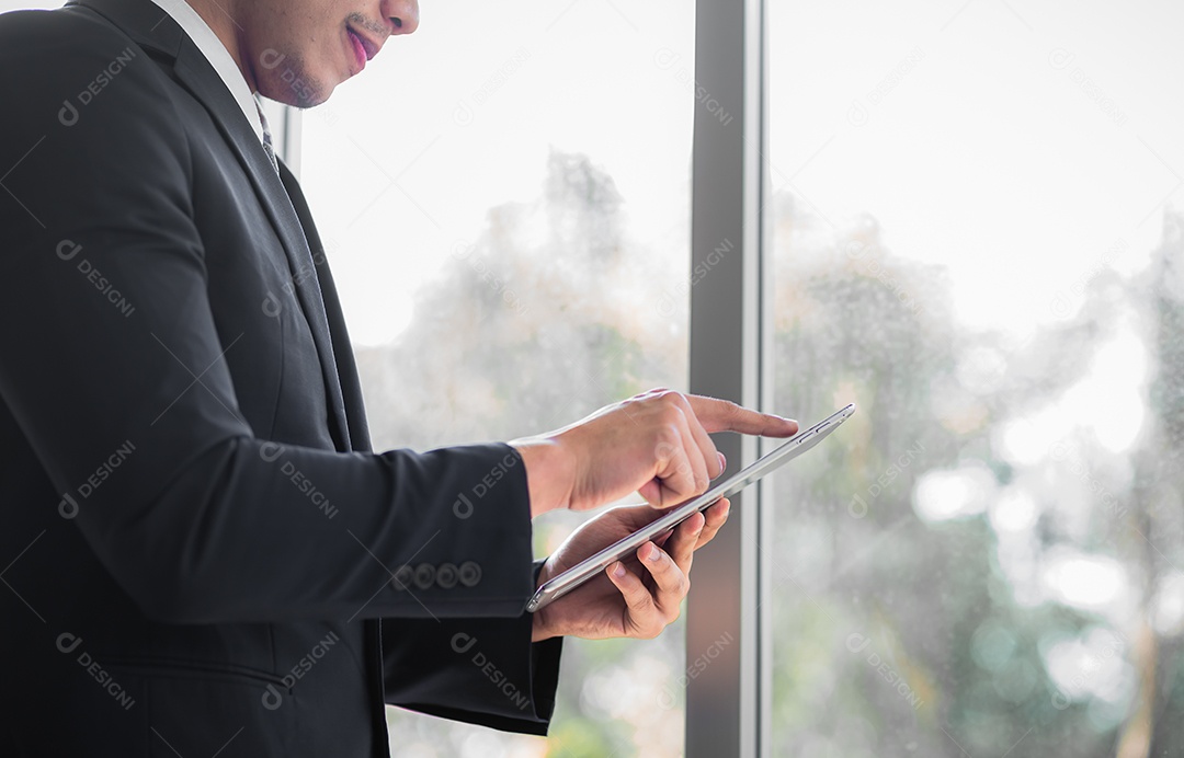 Empresário em pé contemplando enquanto usa tablet