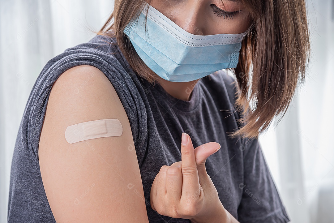 Linda mulher asiática usa máscara e olha o braço depois de receber a vacina
