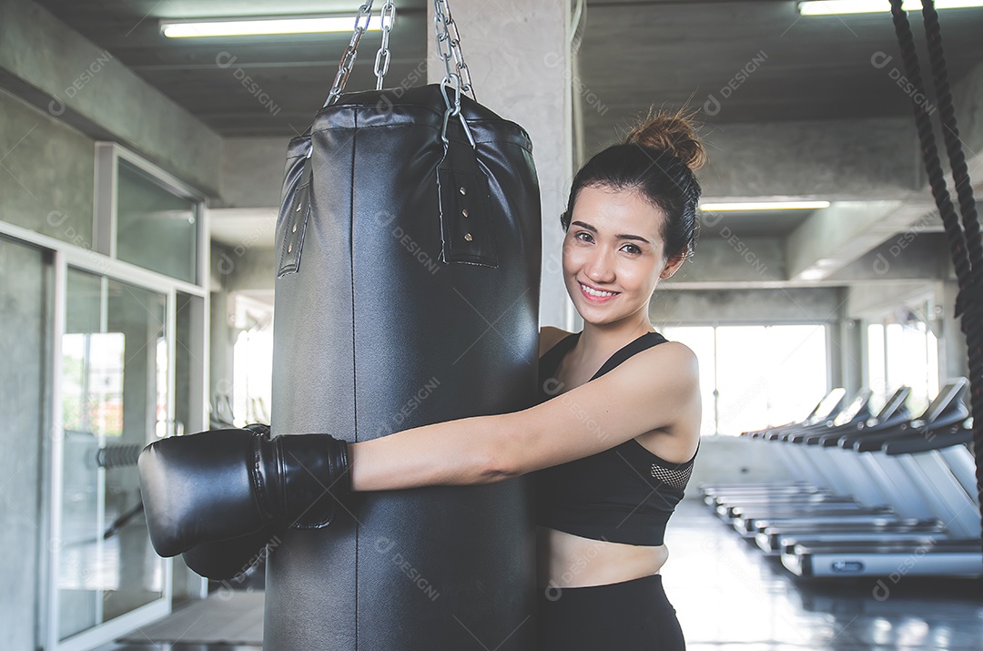 Linda mulher asiática usa luvas de boxe abraçando um saco