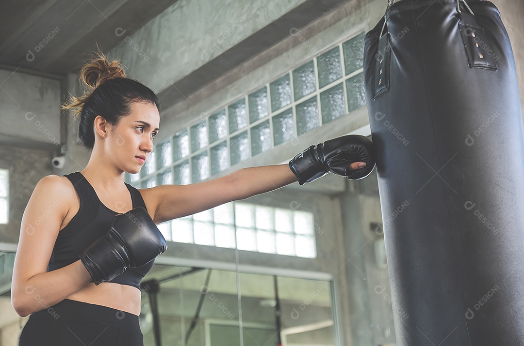 Linda mulher asiática usa luvas de boxe bate saco de areia no ginásio