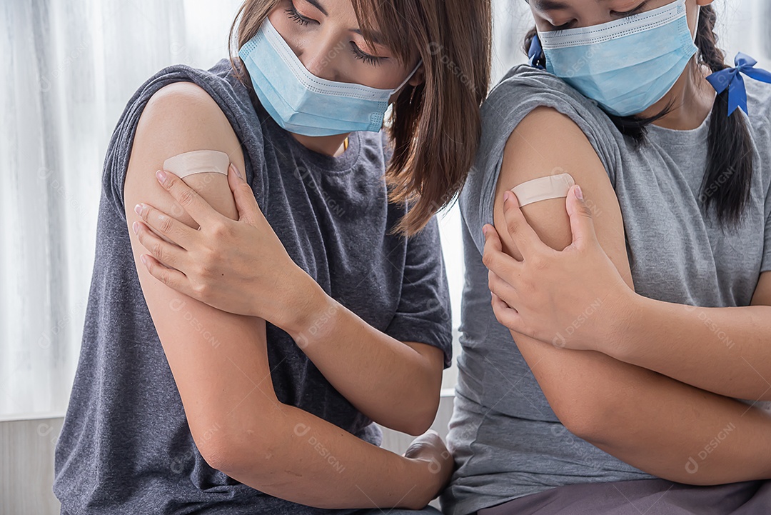 Duas mulheres asiáticas usam máscara e olham o braço depois de receber a vacina