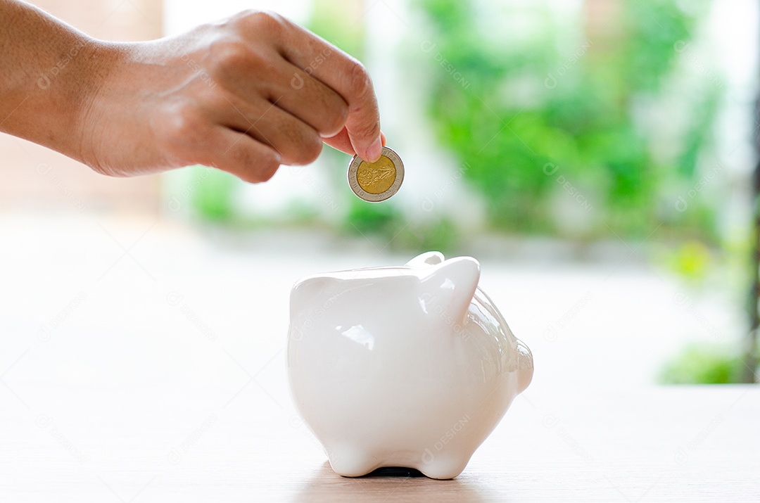 Mão de homem joga moeda no cofrinho