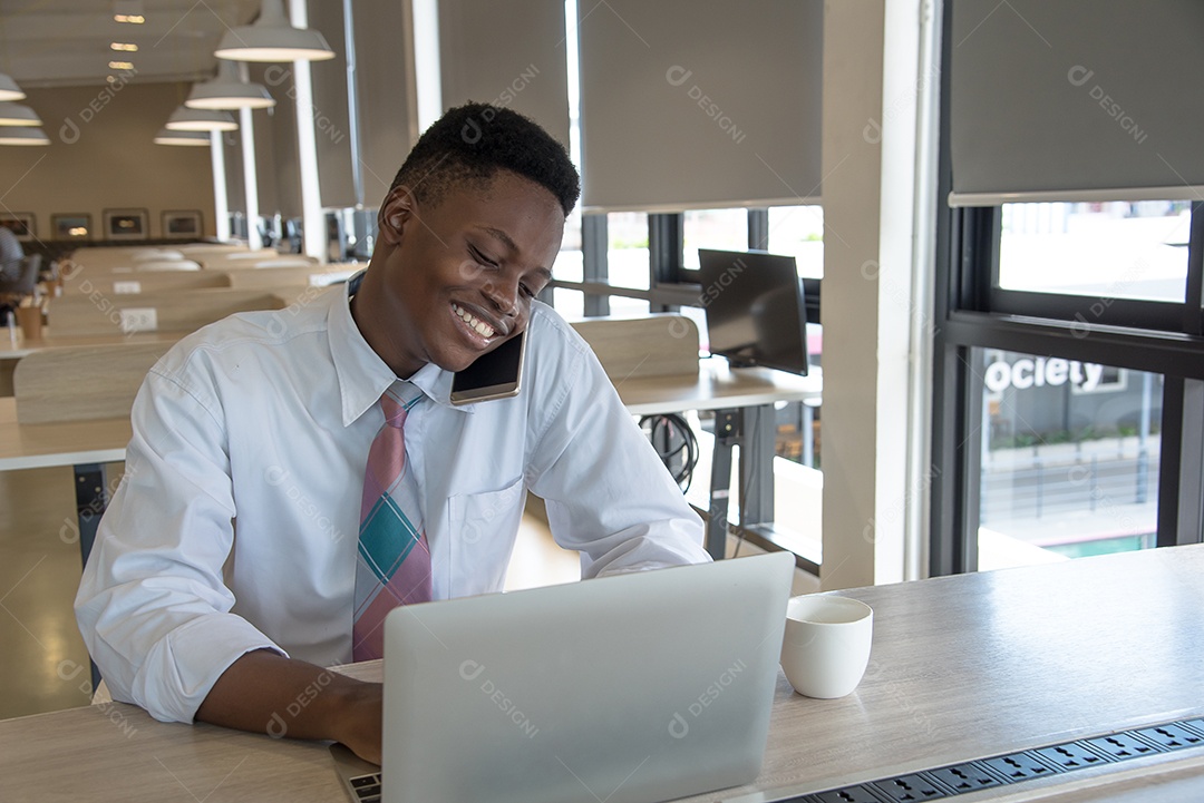 Cara africano usa celular e notebook sorri e feliz