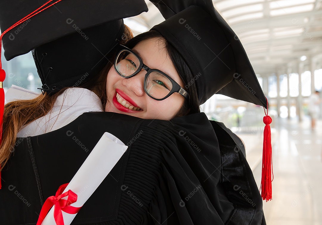 Jovem mulher asiática abraçando sua amiga e se divertindo depois de receber seu certificado de graduação