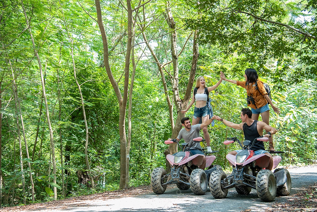 Jovem casal ou amigo alegremente toca suas mãos enquanto monta em um quadriciclo na floresta.