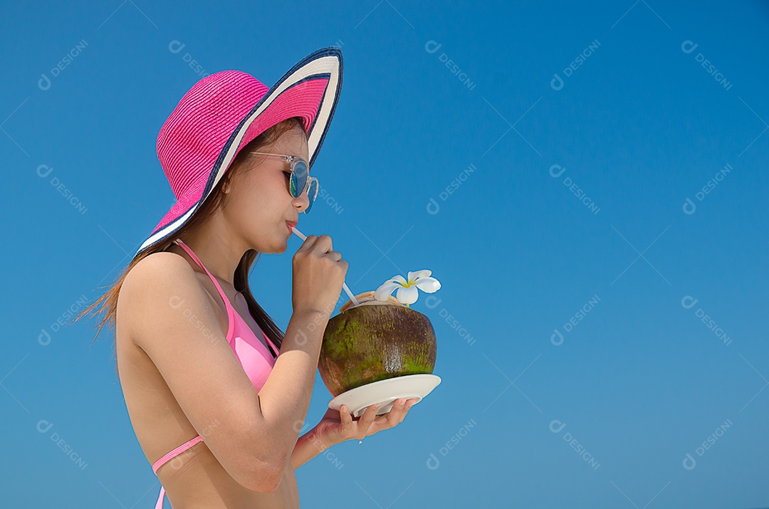 Linda mulher asiática vestindo biquíni rosa e óculos escuros bebendo