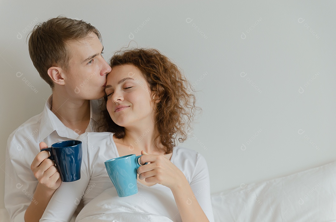 Casal jovem bonito beijou e segurou uma caneca de café na cama