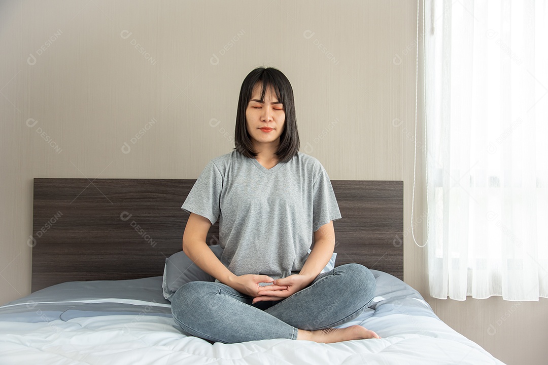 A mulher asiática está meditando na cama