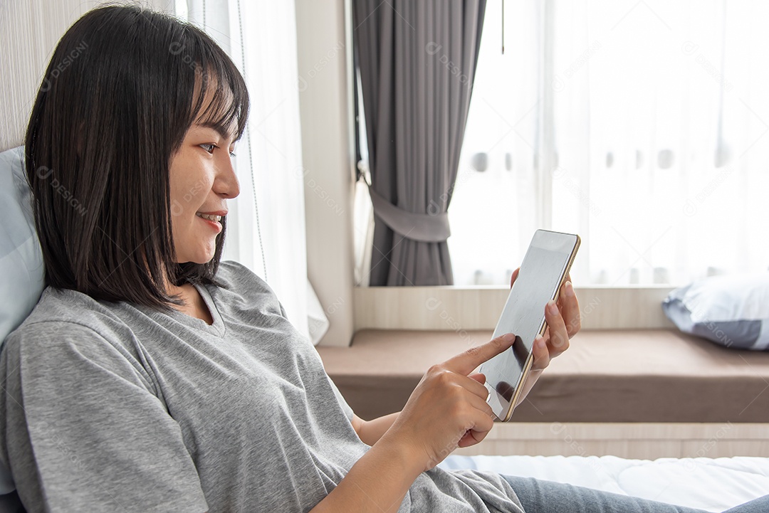 Mulher asiática toca tablet na cama e sorri