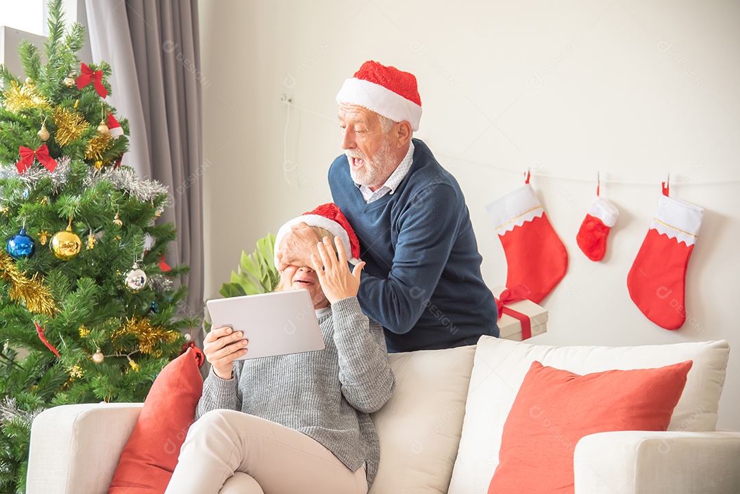 Marido mais velho dá uma caixa de presente para sua esposa sentado no sofá e usando um chapéu