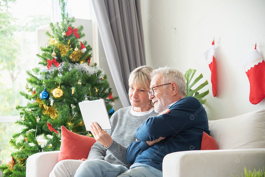 Casal idosos sentou-se e olhou para tablet na sala de estar com uma árvore de natal