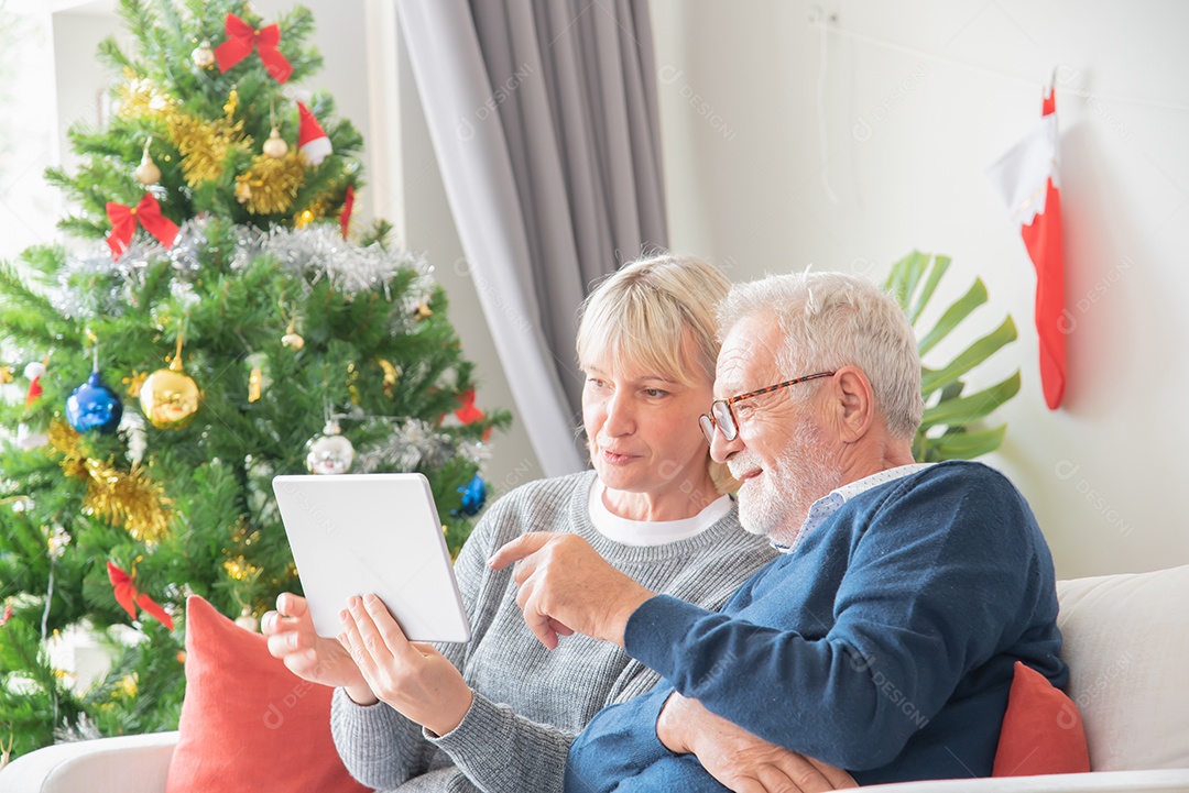 Casal idosos sentou-se e olhou para tablet na sala de estar com uma árvore de natal