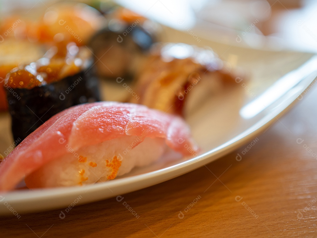 Vários sushi em um prato branco colocado sobre uma mesa de madeira.