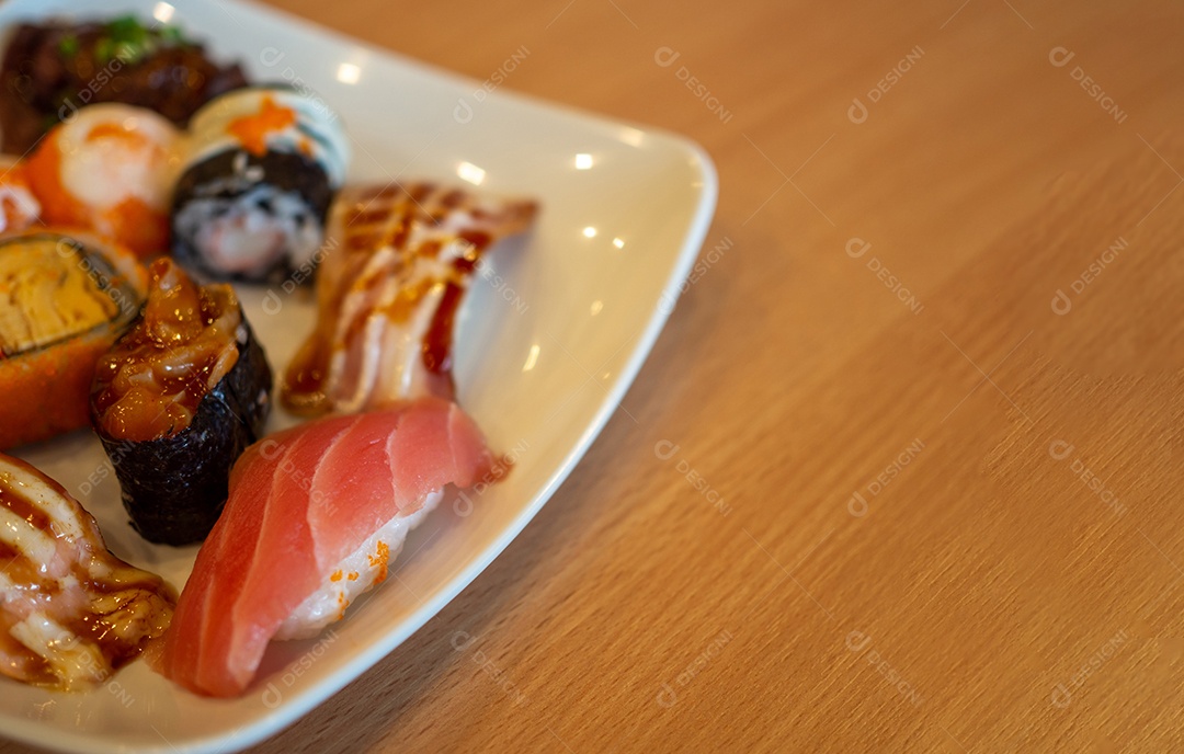 Vários sushi em um prato branco colocado sobre uma mesa de madeira.