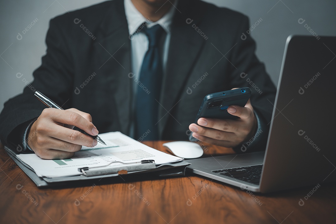 Mão de empresário segurando o celular e caneta com documentos de negócios de gráficos e gráficos na mesa. Calculadora e computador para investimento e análise econômica. Conceito de negócios financeiros e fiscais.