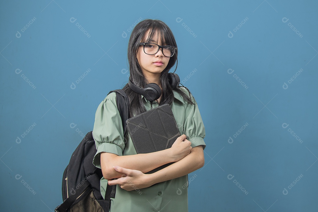 Mulher asiática vestindo uma mochila verde e segurando um tablet com fones de ouvido