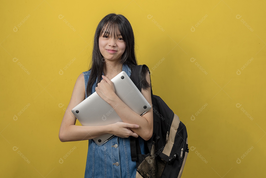 Pessoa asiática adolescente vestindo jeans segurando o laptop do computador no fundo.