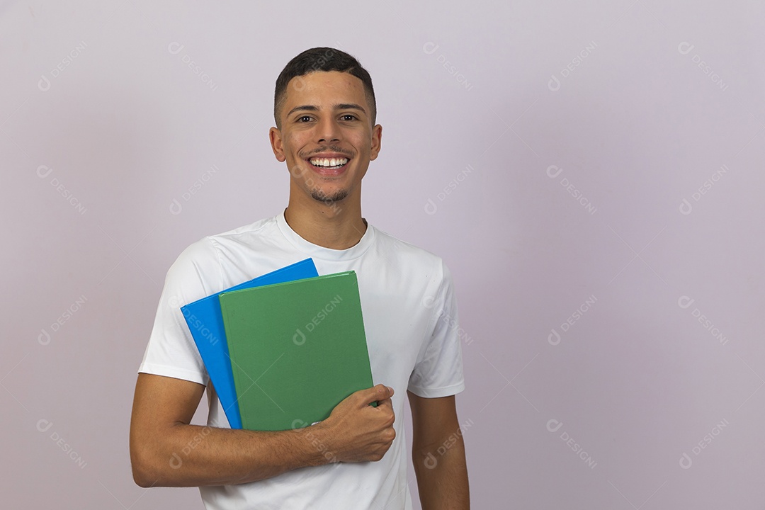 Homem jovem brasileiro estudante segurando materiais escolar sorridente sobre fundo isolado branco