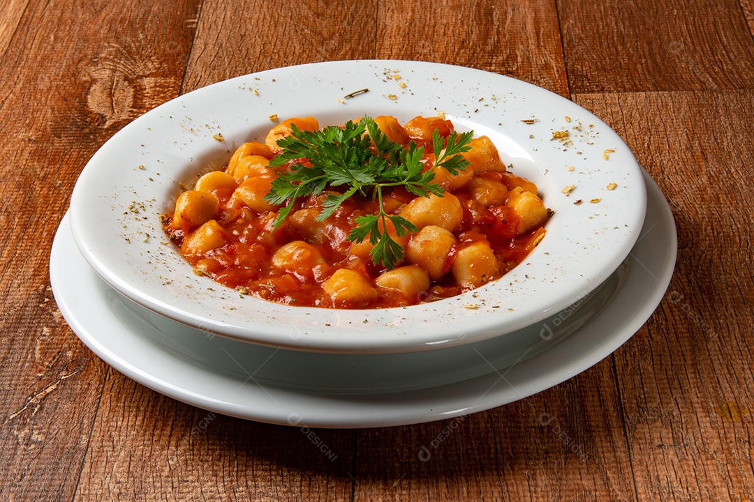 Prato de nhoque com molho de tomate e salsa na mesa de madeira rústica