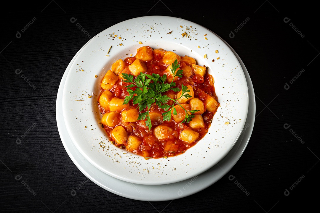 Prato de nhoque com molho de tomate e salsa na mesa de madeira rústica