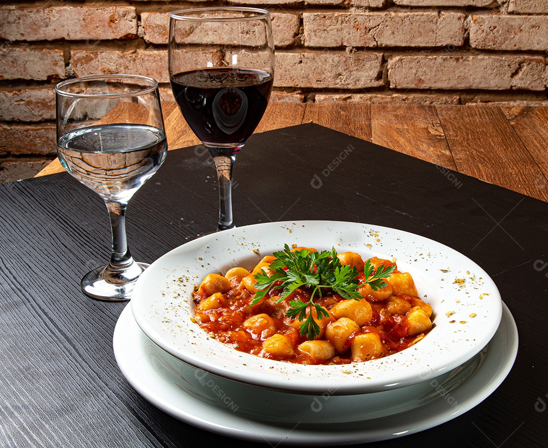 Prato de nhoque com molho de tomate e salsa na mesa de madeira rústica