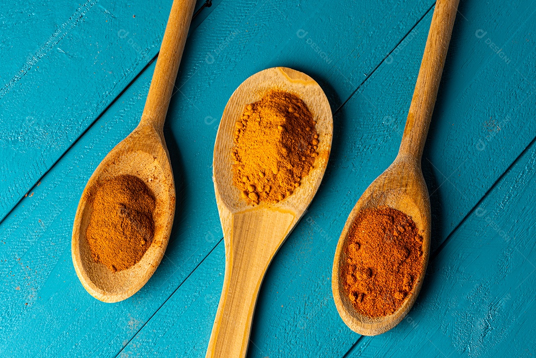Colheres de pau com especiarias em uma mesa de madeira rústica azul.