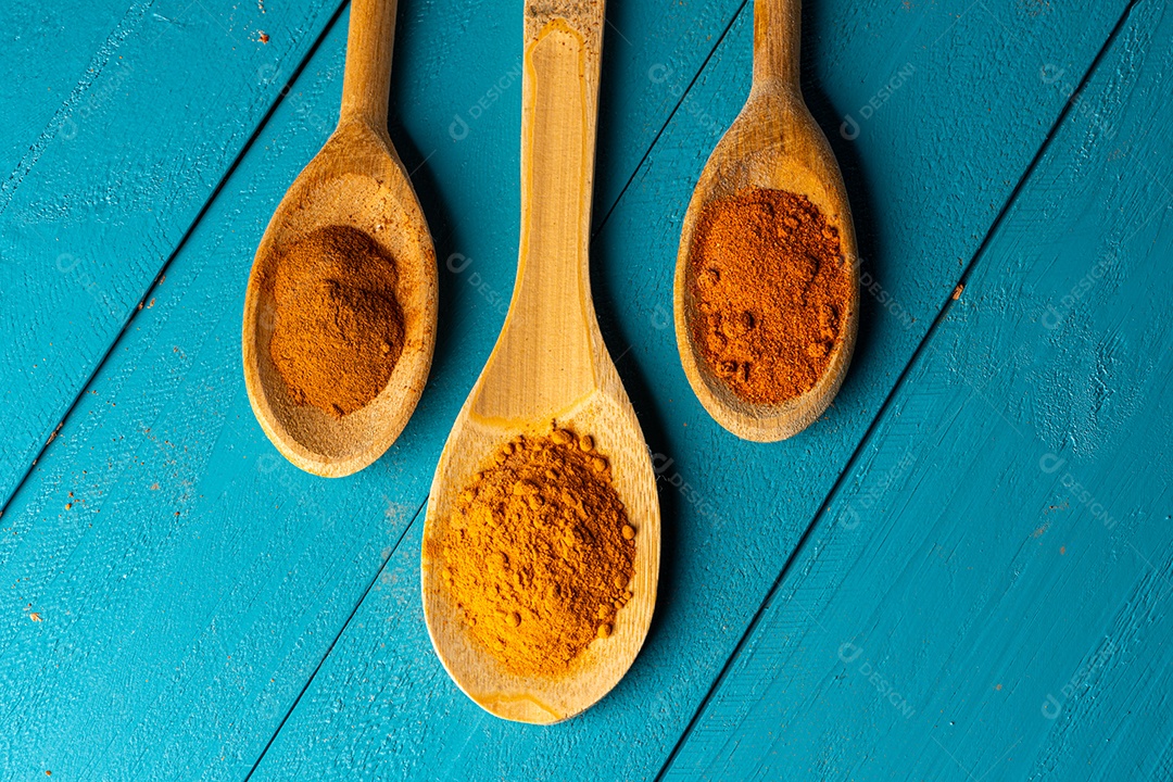 Colheres de pau com especiarias em uma mesa de madeira rústica azul.