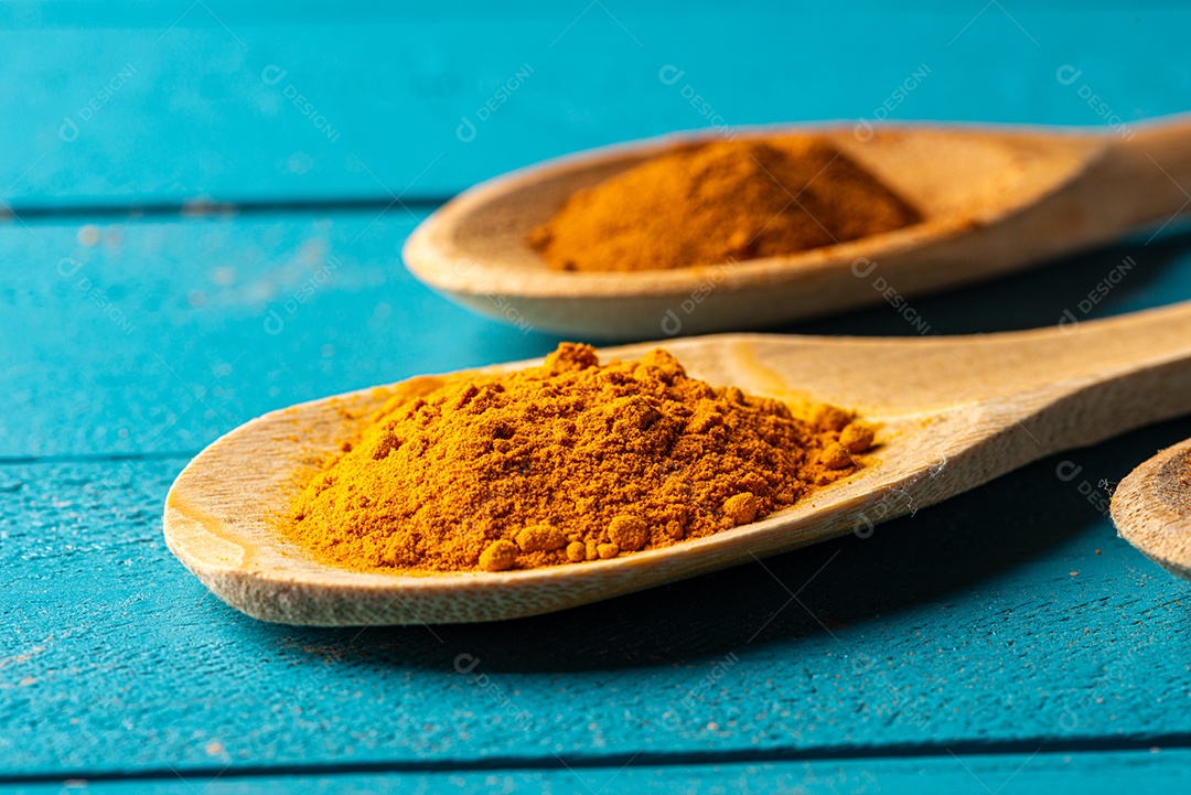 Colheres de pau com especiarias em uma mesa de madeira rústica azul.