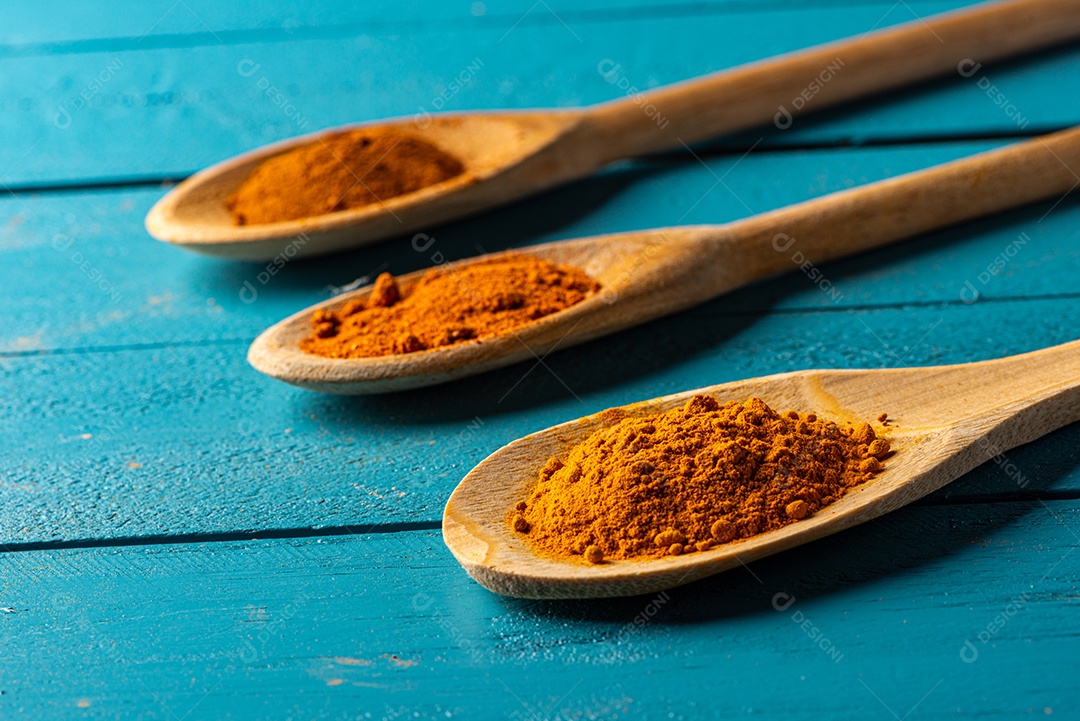 Colheres de pau com especiarias em uma mesa de madeira rústica azul.