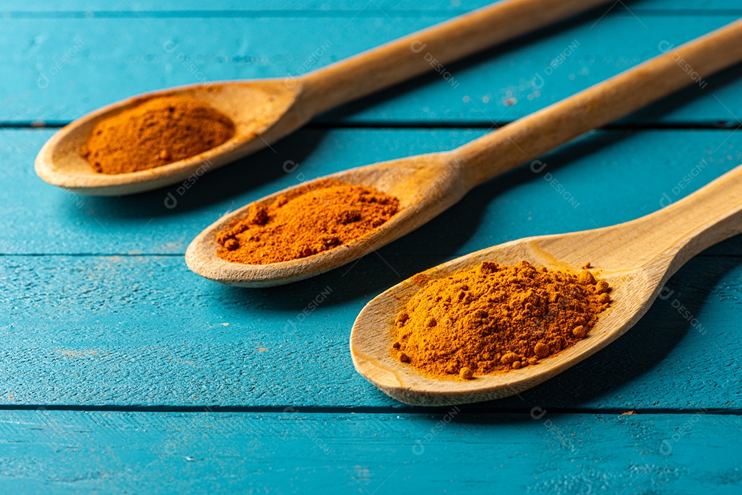 Colheres de pau com especiarias em uma mesa de madeira rústica azul.