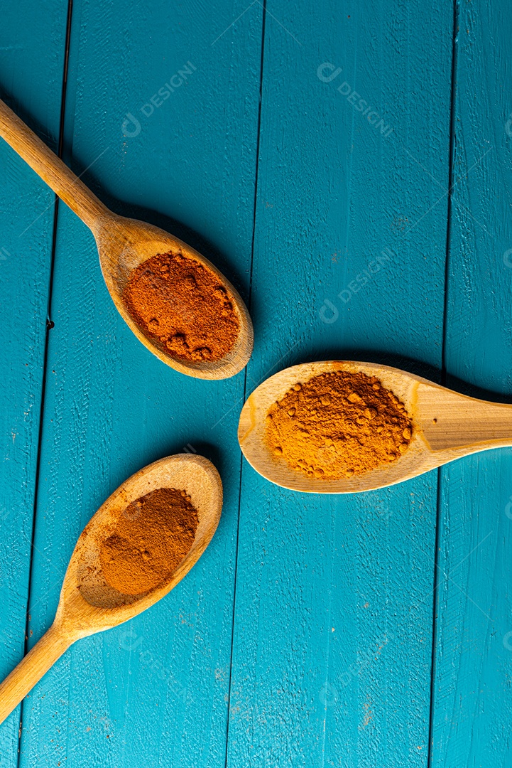 Colheres de pau com especiarias em uma mesa de madeira rústica azul.