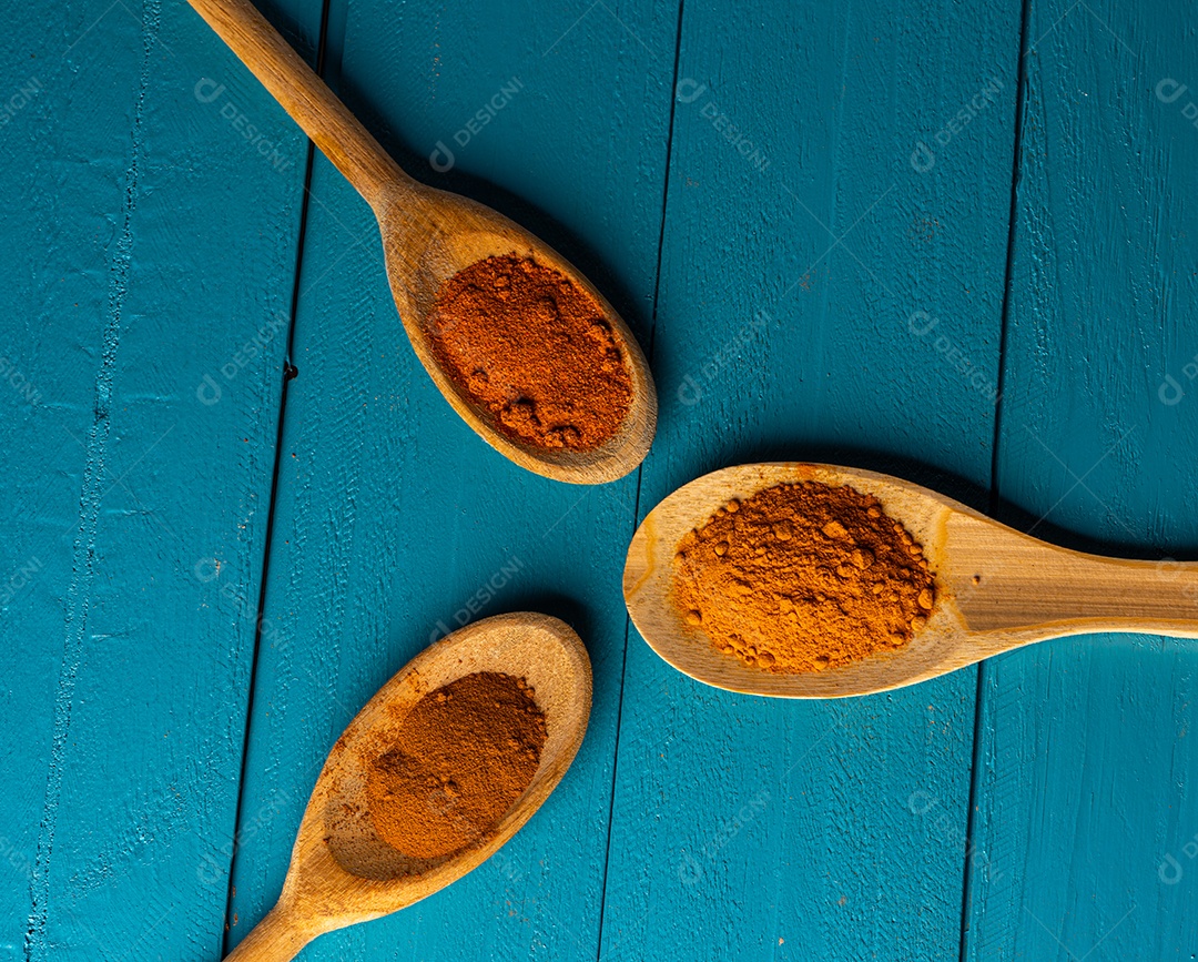 Colheres de pau com especiarias em uma mesa de madeira rústica azul.