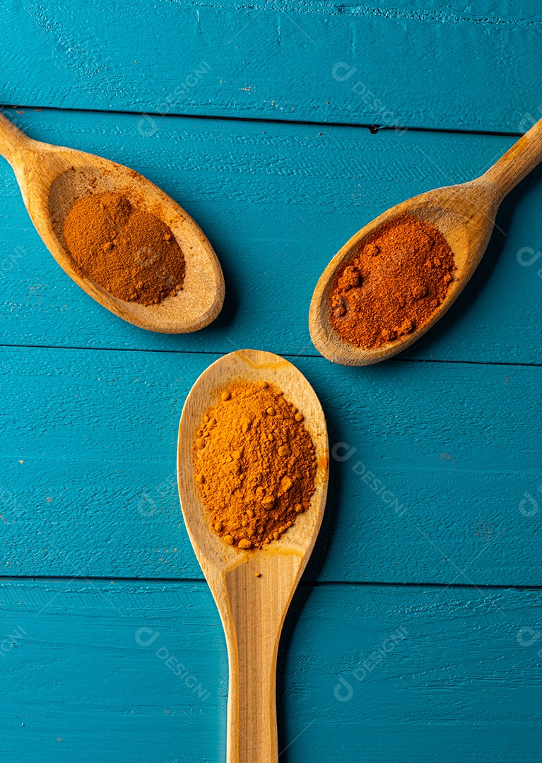Colheres de pau com especiarias em uma mesa de madeira rústica azul.