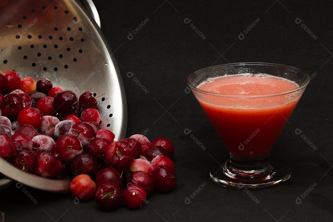 Tigela cheia de acerolas frescas ao lado de suco de acerola