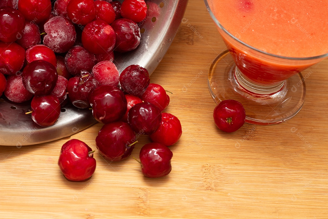 Tigela cheia de acerolas frescas ao lado de suco de acerola