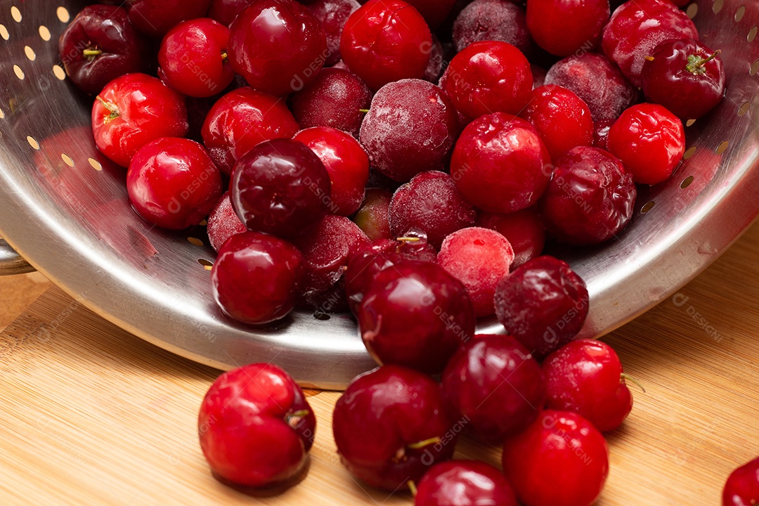 Tigela cheia de acerolas frescas ao lado de suco de acerola