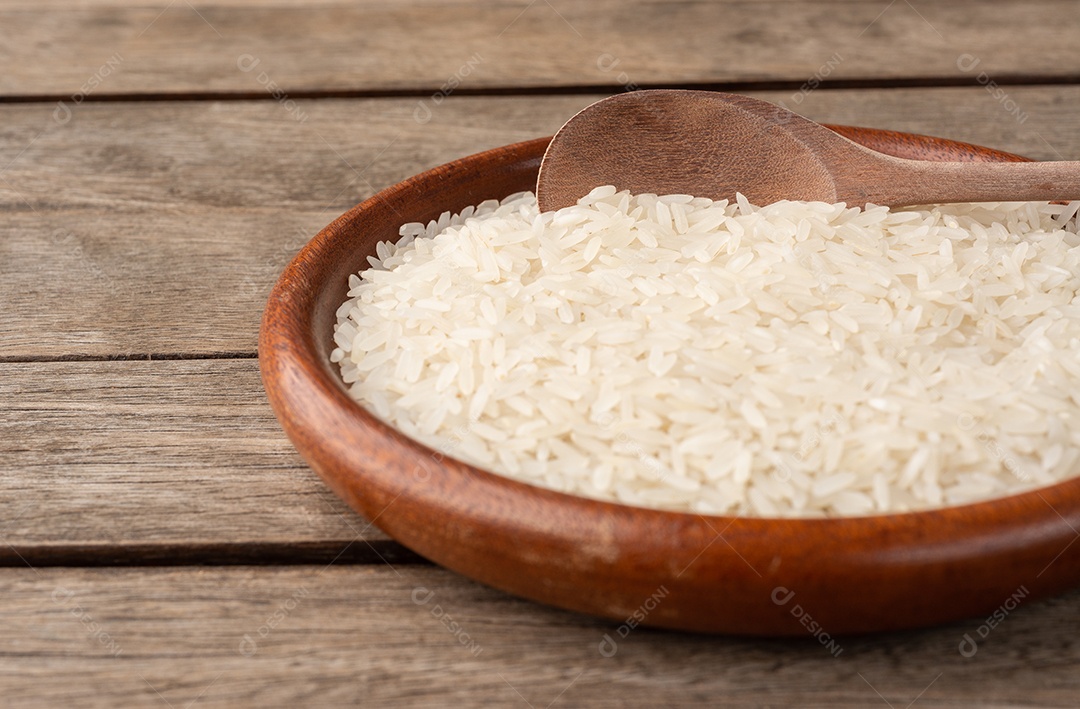 Arroz branco cru em um prato sobre mesa de madeira com espaço de cópia.