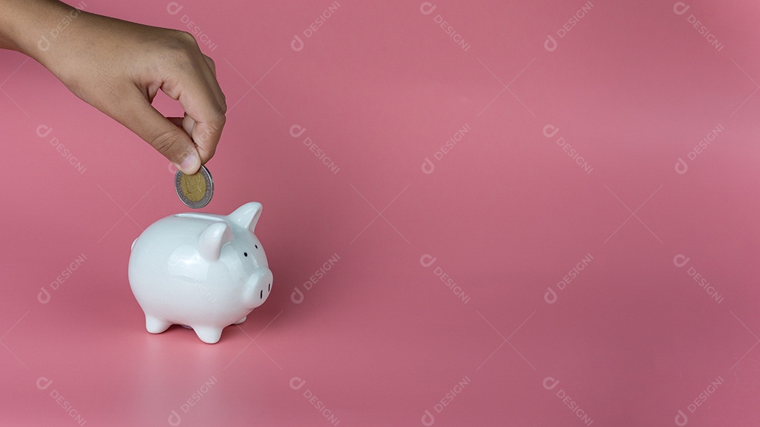 Uma mão humana colocou uma moeda em um cofrinho em um fundo rosa.