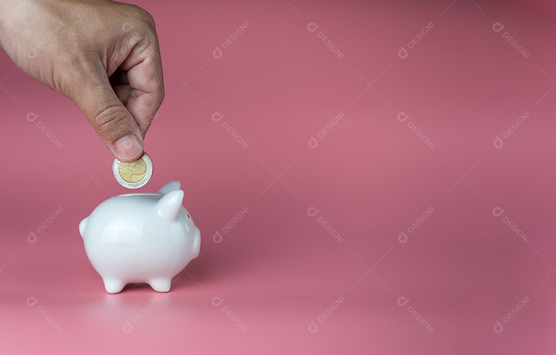 Uma mão humana colocou uma moeda em um cofrinho em um fundo rosa.