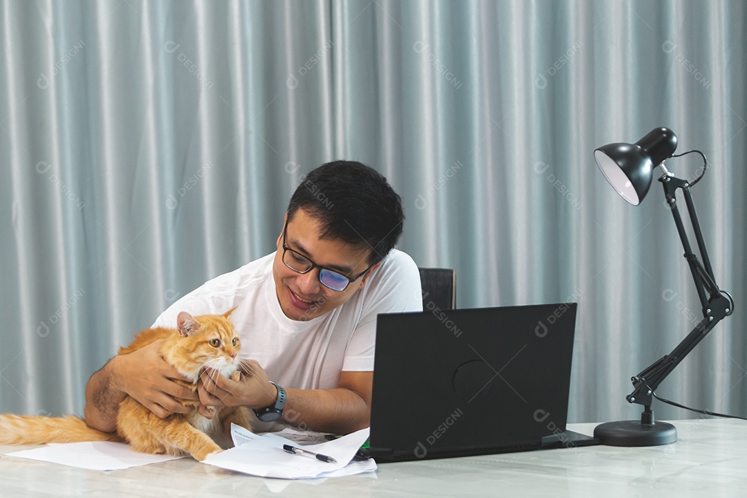 Homem segurando seu gato de estimação sobre escritório mexendo notebook