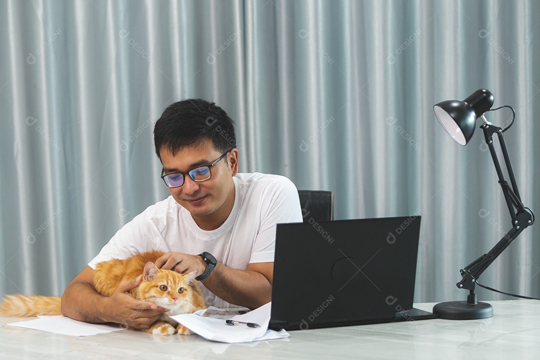 Homem segurando seu gato de estimação sobre escritório mexendo notebook
