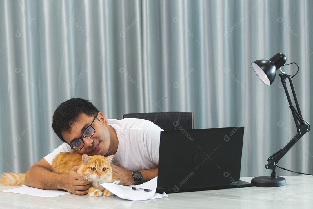 Homem segurando seu gato de estimação sobre escritório mexendo notebook