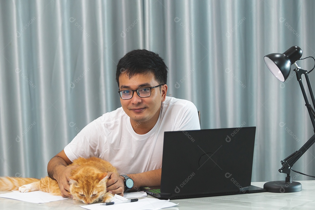 Homem segurando seu gato de estimação sobre escritório mexendo notebook