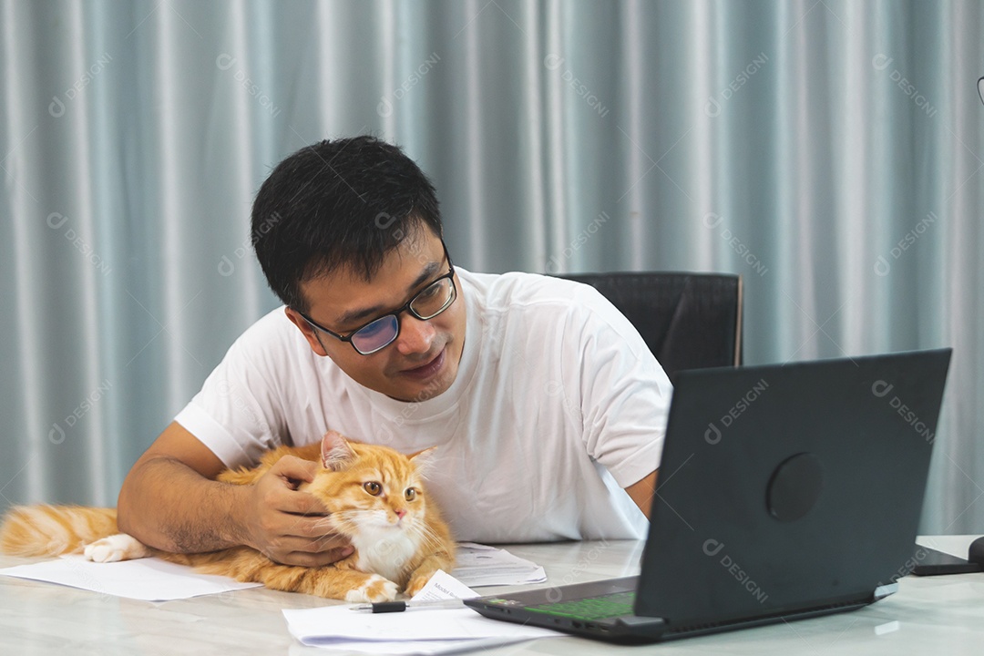 Homem segurando seu gato de estimação sobre escritório mexendo notebook