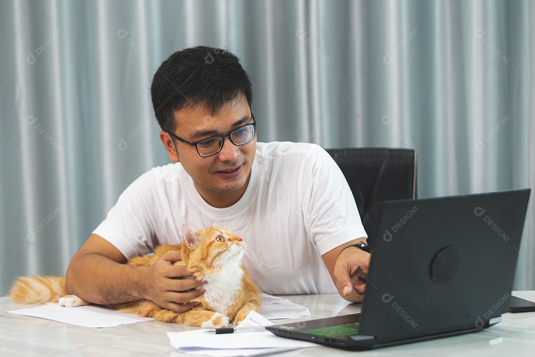Homem segurando seu gato de estimação sobre escritório mexendo notebook