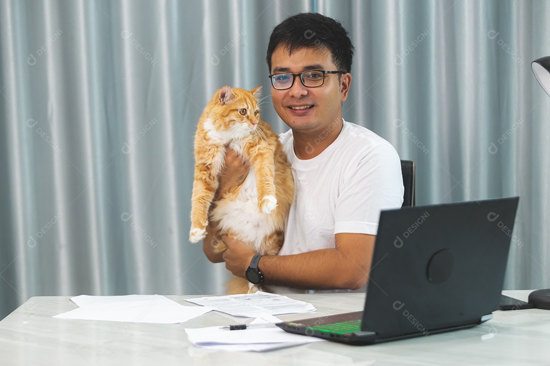 Homem segurando seu gato de estimação sobre escritório mexendo notebook