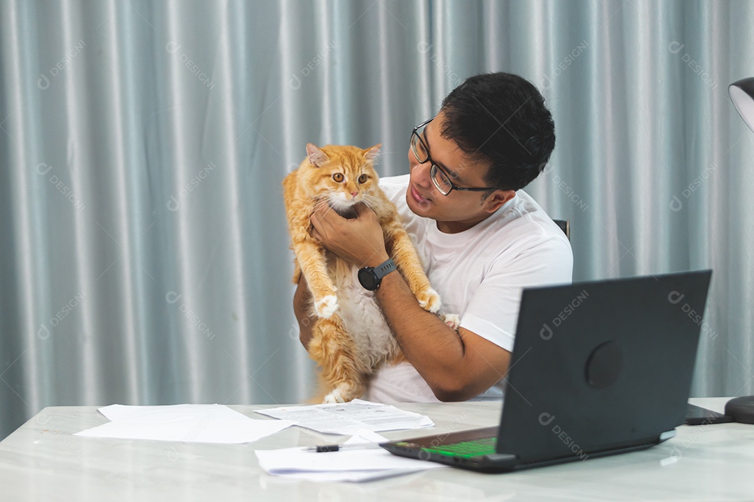 Homem segurando seu gato de estimação sobre escritório mexendo notebook