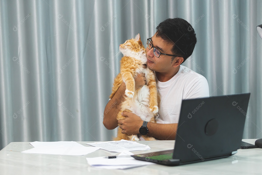 Homem segurando seu gato de estimação sobre escritório mexendo notebook