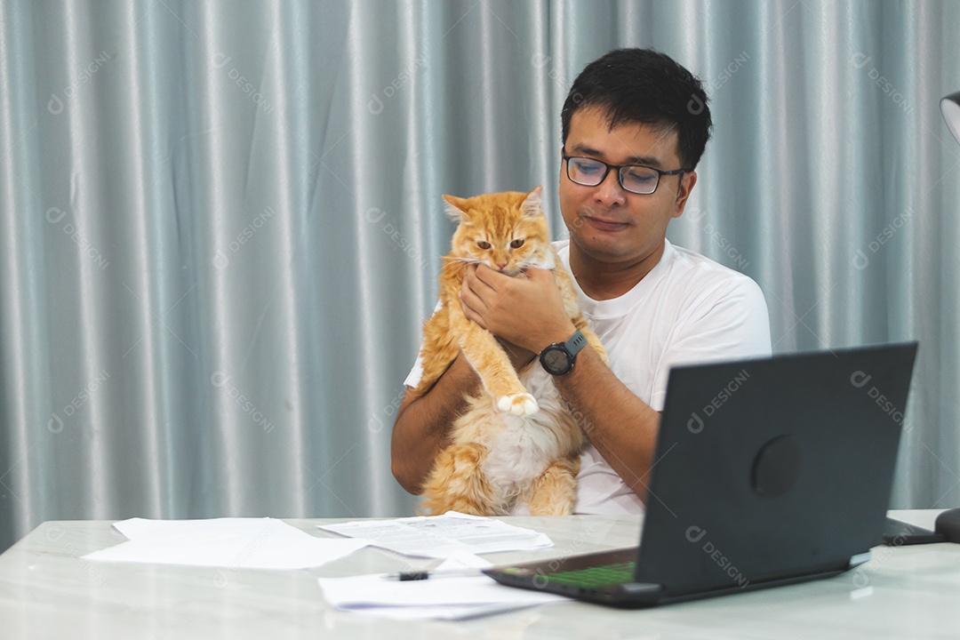 Homem segurando seu gato de estimação sobre escritório mexendo notebook