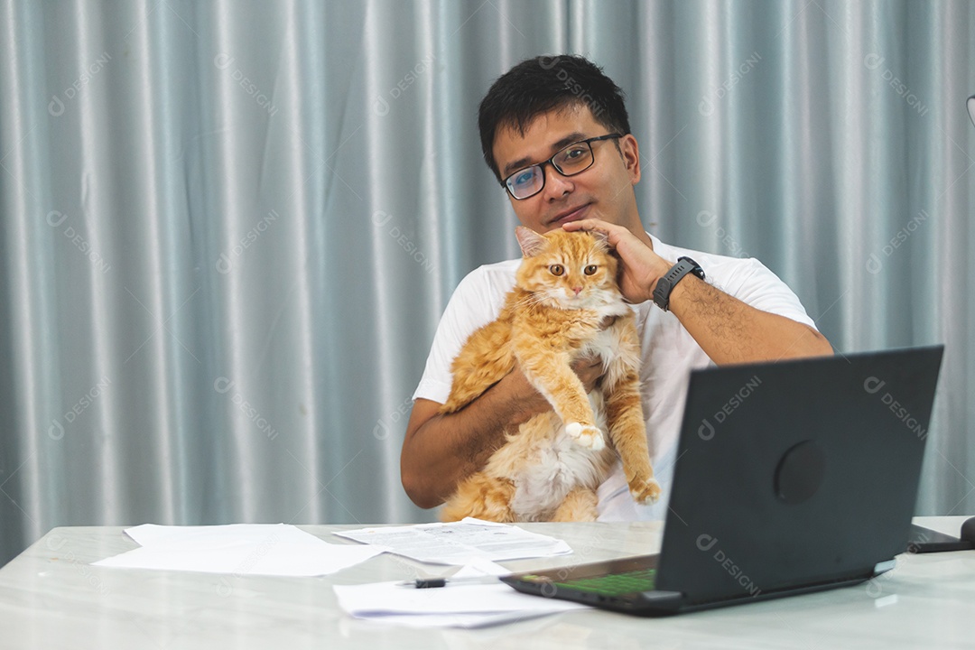 Homem segurando seu gato de estimação sobre escritório mexendo notebook